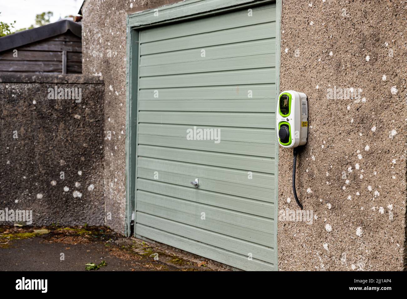 Seitenansicht eines Garagentors und eines an der Wand montierten Rolec EV Wallpod, eines Elektrofahrzeugs oder Steckers. Cardross, Argyll and Bute, Schottland, Großbritannien, 06-30-2022 Stockfoto