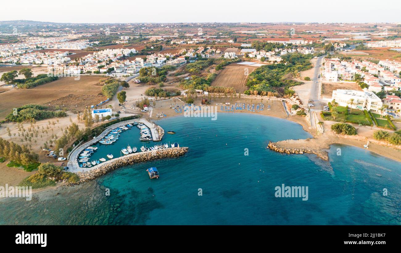 Luftbild des Sonnenuntergangs an der Küste und die weiße, gewaschene Kapelle am Strand Agia Triada, Protaras, Famagusta, Zypern von oben. Vogelperspektive auf Tour Stockfoto