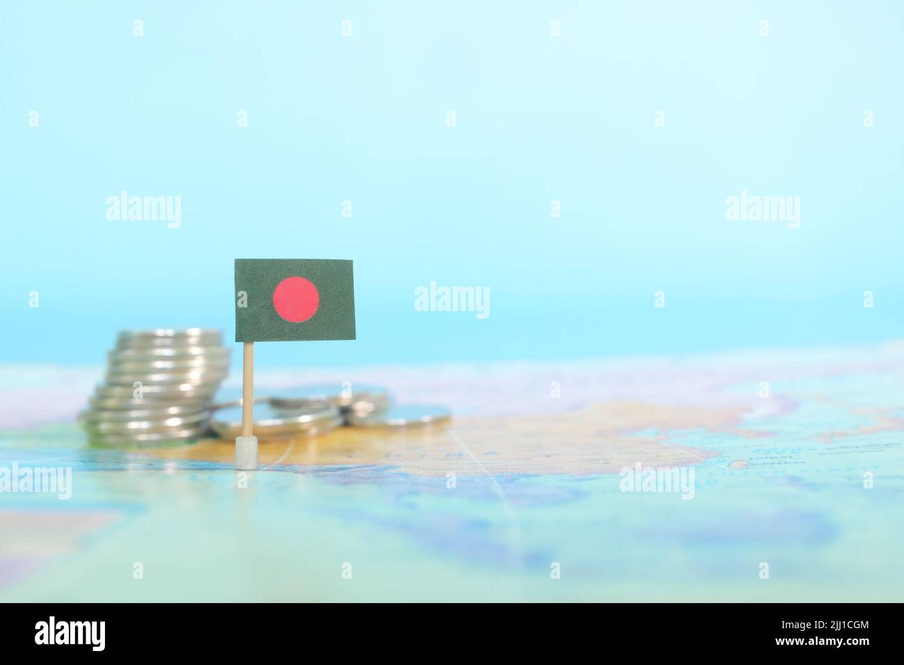 Selektiver Fokus der Bangladesh-Flagge auf verschwommener Weltkarte mit Münzen. Bangladesh Wirtschaft und Wohlstand Konzept. Stockfoto
