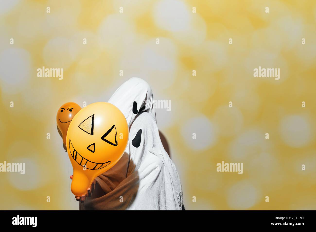 Frohe Halloween. Verängstigte Geister umarmen sich vor hellem, gelb schimmerndem Hintergrund. Die Kinder sind in weiße Kostüme gekleidet und mit orangefarbenen Luftballons bemalt. Kostüme werden von Hand gefertigt. Home Rest-Konzept Stockfoto