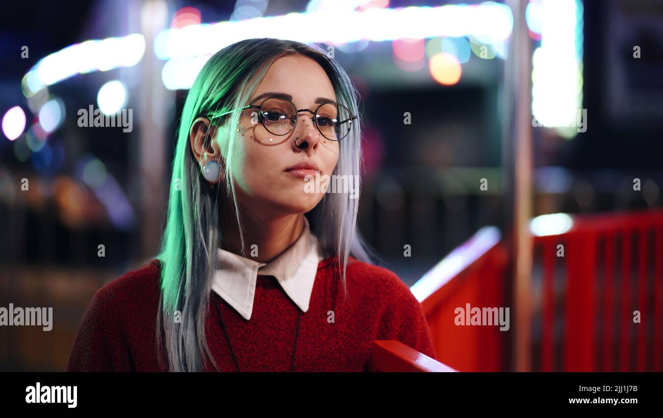 Hipster-Mädchen mit blau gefärbten Haaren, goldenen Pailletten als Sommersprossen. Frau mit Nasenpiercing, transparente Brille, Ohrentunnel, ungewöhnliche Frisur steht in Stockfoto