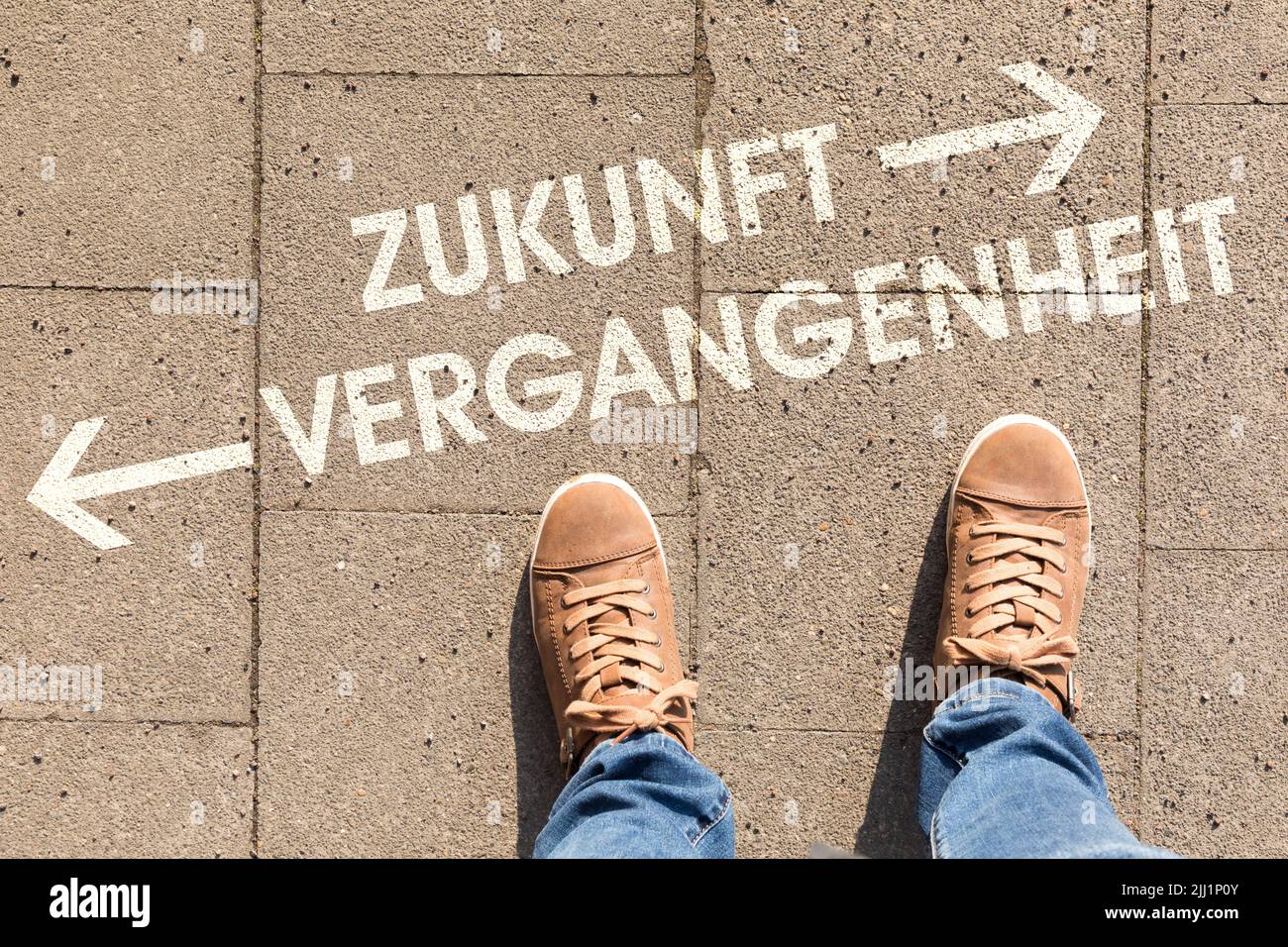 Ein brauner Schuh mit Text, der auf deutsch auf einem Boden die Richtung in die Zukunft oder Vergangenheit zeigt Stockfoto