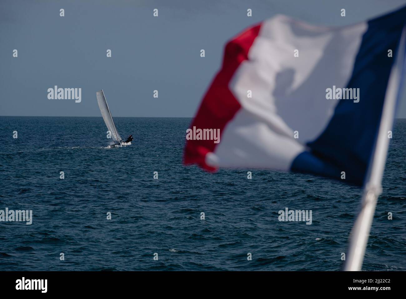 Die französische Flagge, blau-weiß-rot, hängt an einem Boot, ein Segelboot fährt vorbei, es ist das offene Meer. Stockfoto