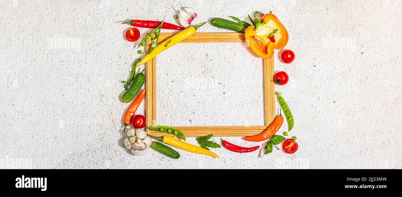 Verschiedene frische Gemüse und Gewürze rund um den Holzrahmen. Reife gelbe Paprika, Tomate, Erbse, Gurke, Knoblauch, Bunte Chilischoten. Zutaten zum Kochen Stockfoto