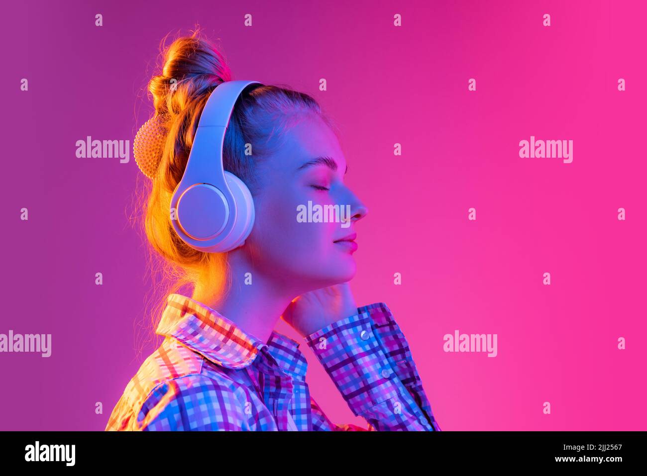 Porträt von entzückenden jungen Mädchen, Student trägt kariertes Hemd isoliert auf magentafarbenen Hintergrund in Neonlicht. Konzept von Schönheit, Kunst, Mode Stockfoto