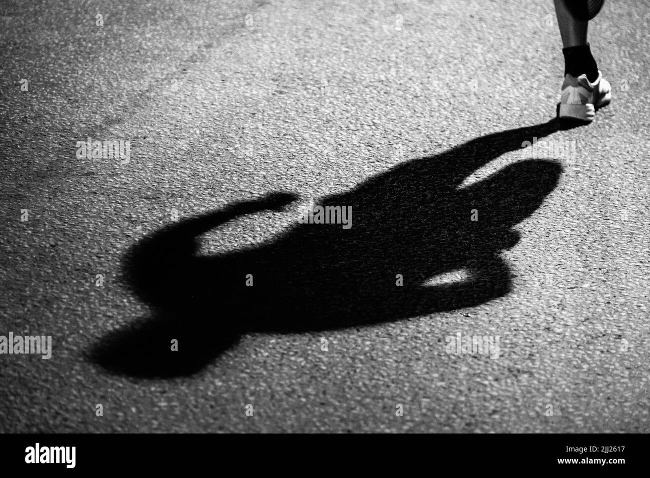 Schatten des Läufers auf dunklem Asphalt in der Nacht Stockfoto