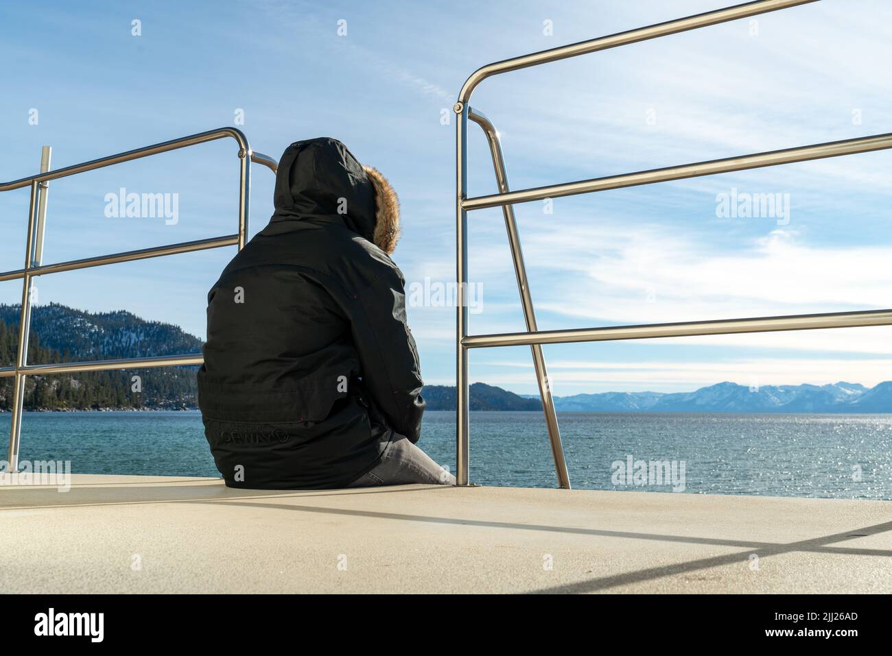 Der Rettungsschwimmer sitzt in einer warmen Kapuzenjacke auf dem Wachturm des Rettungsschwimmern am Strand und beobachtet das Meer bei kaltem Wetter Stockfoto