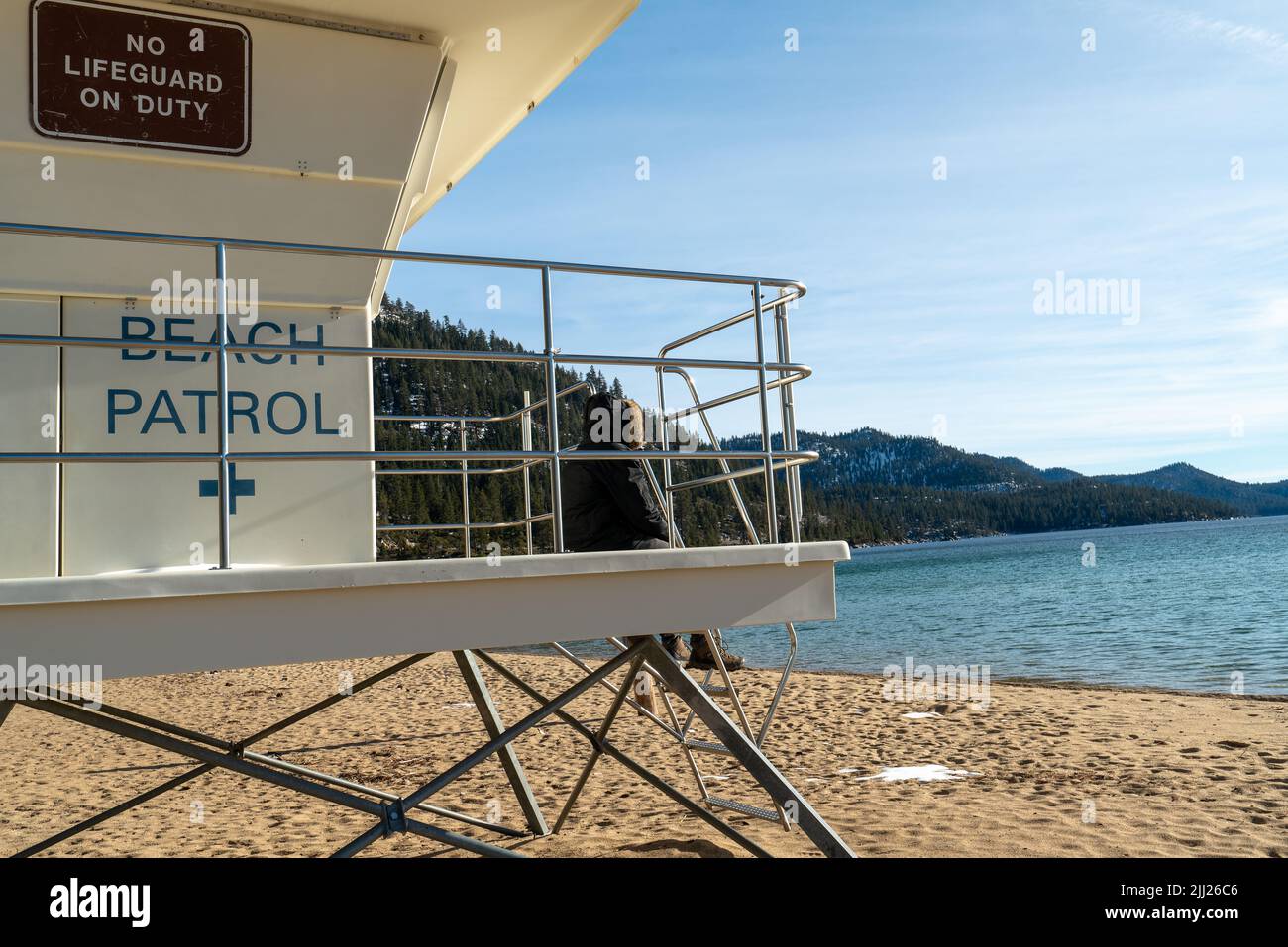 Der Rettungsschwimmer sitzt in einer warmen Kapuzenjacke auf dem Wachturm des Rettungsschwimmern am Strand und beobachtet das Meer bei kaltem Wetter Stockfoto