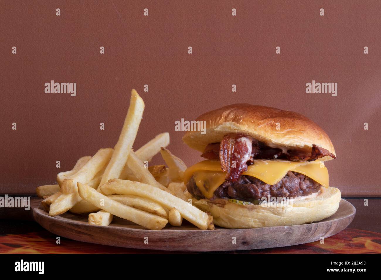 Rinderburger mit Käse in Scheiben, gebratenem Speck und pommes auf Holzplatte Stockfoto