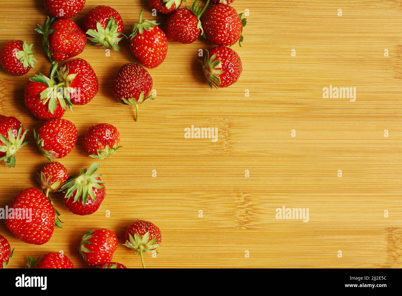 Frische, saftige Bio-Erdbeeren mit Blättern in der runden Glasschale, die auf das Holz-Bambus-Schneidebrett gelegt wird. Zutaten für Marmelade, Kuchen, Dess Stockfoto