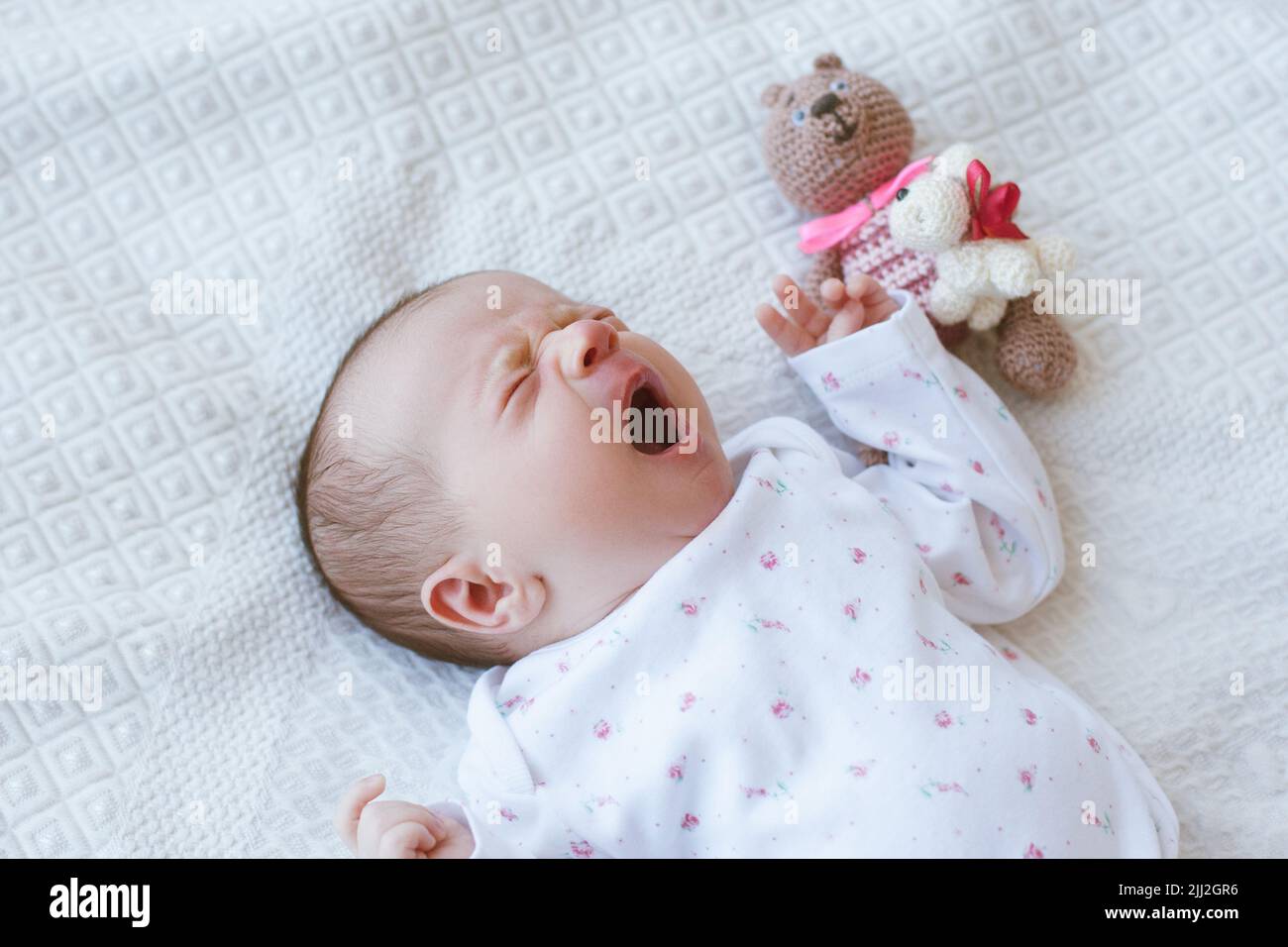 Ein verschlaftes Neugeborenes gähnt süß auf dem Bett Stockfoto