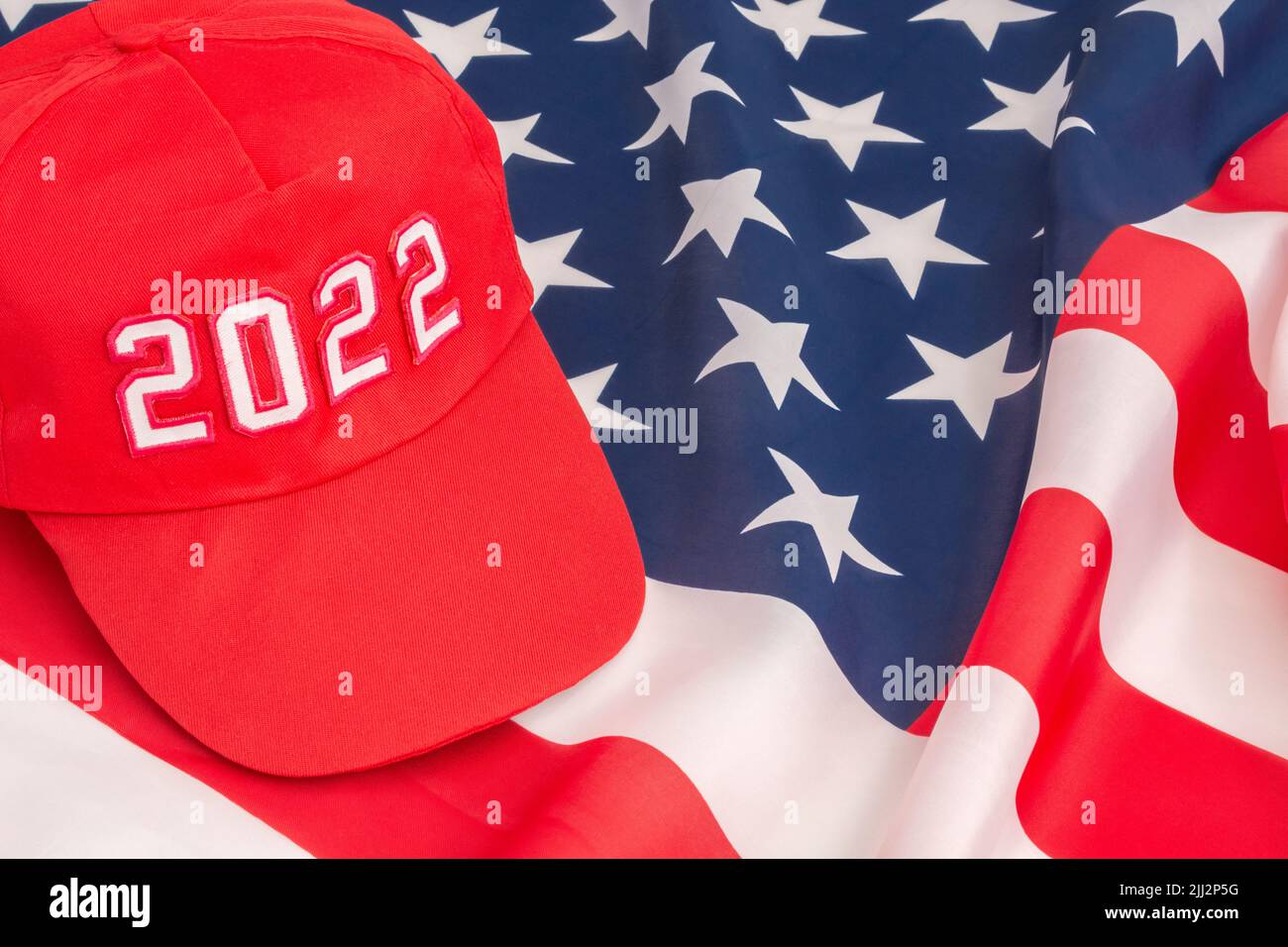 Rote MAGA-Kappe mit Datum 2022 und US Stars and Stripes-Flagge. Für die US-Zwischenwahlen vom 2022. November und die Ausrottung der Demokraten durch die US-Republikaner der Roten Welle. Stockfoto