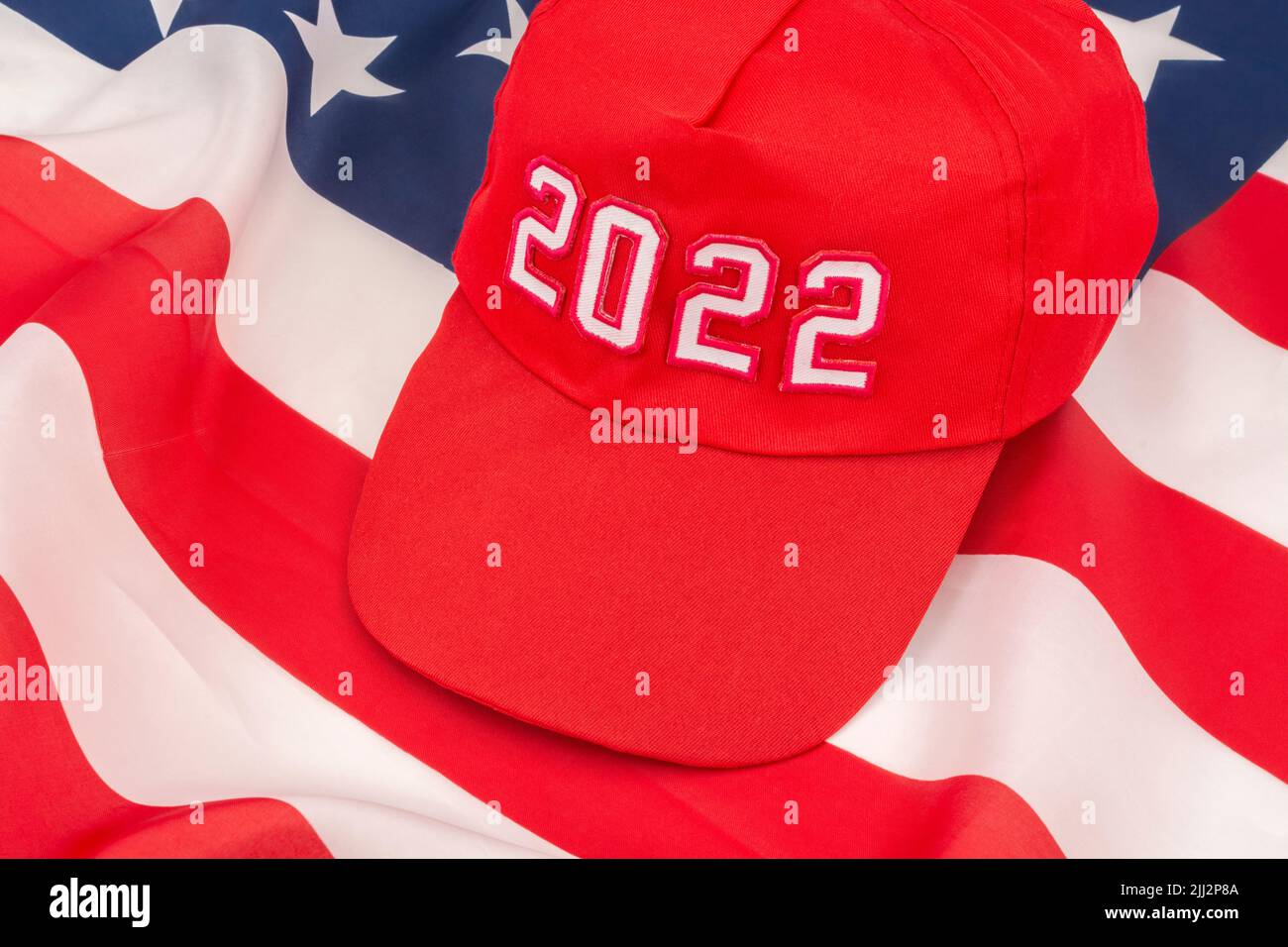 Rote MAGA-Kappe mit Datum 2022 und US Stars and Stripes-Flagge. Für die US-Zwischenwahlen vom 2022. November und die Ausrottung der Demokraten durch die US-Republikaner der Roten Welle. Stockfoto