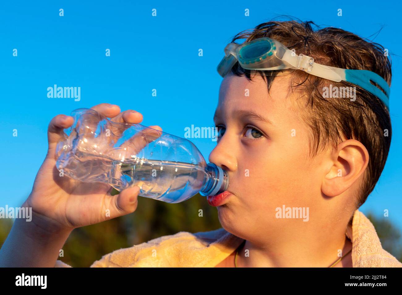 Glücklicher Junge in den Schwimmgläsern trinkt Wasser aus einer Flasche am Strand Stockfoto