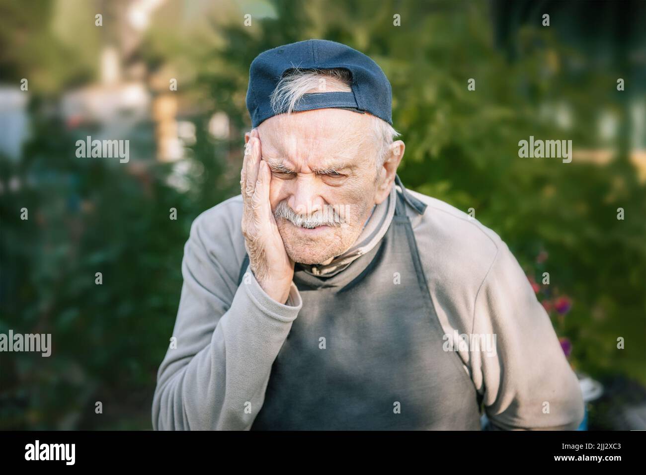 Porträt eines 88-jährigen Mannes mit Kopfschmerzen oder Zahnschmerzen. Bauer arbeitet im Garten. Kopierraum Stockfoto