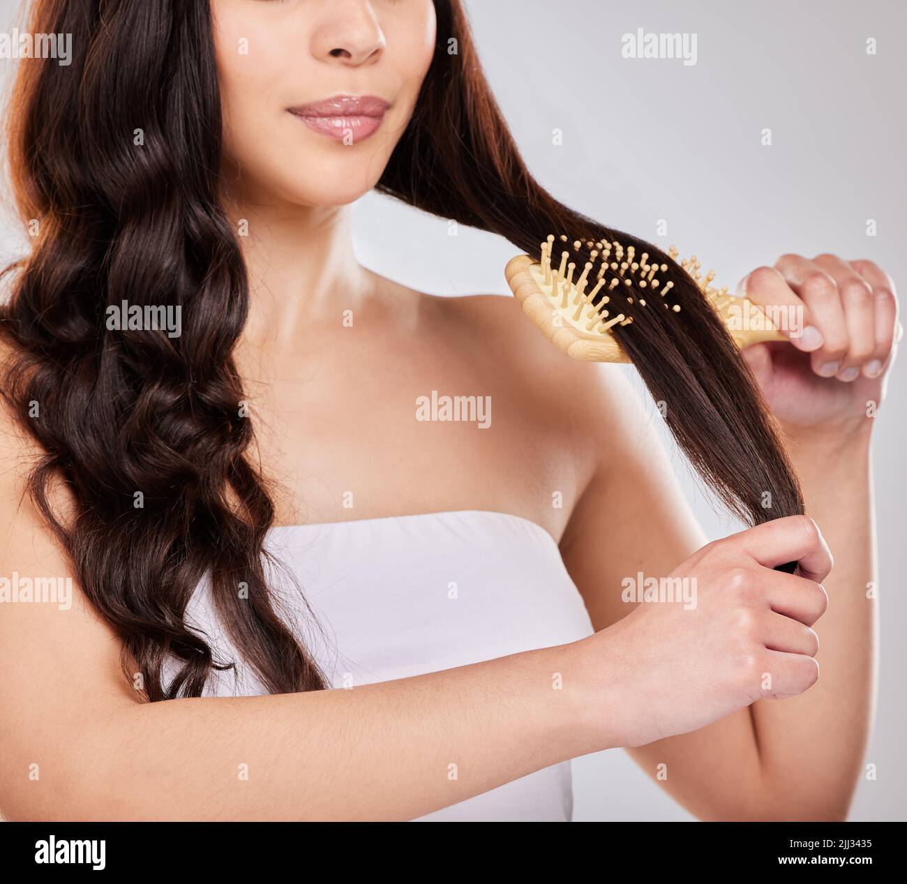 Tragen Sie einen Hitzeschutz auf und stylen Sie Ihr Haar, wie Sie möchten. Studioaufnahme einer jungen Frau, die sich die Haare putzt. Stockfoto