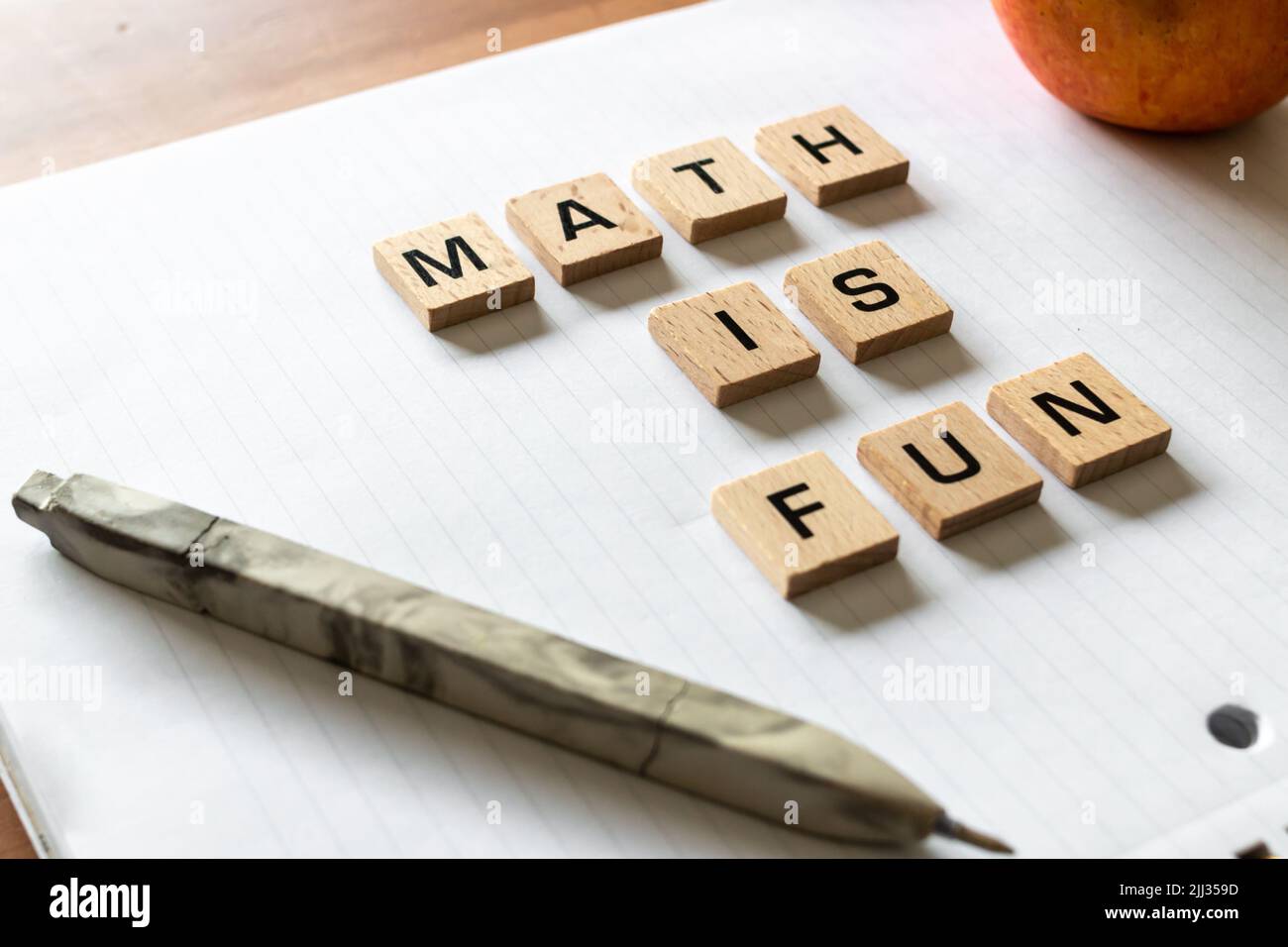 ​ Holzbuchstaben buchstabieren „math is fun“ auf einem weißen, weißen Notizblock neben einem roten Apfel und einem Stift. Schreibtischoberfläche aus Hartholz. Lernen. Stockfoto