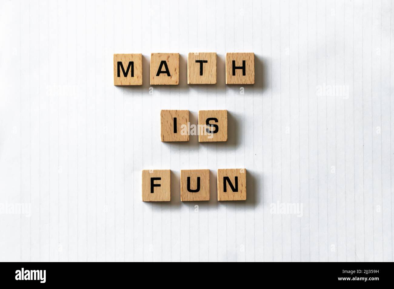 ​ Holzbuchstaben buchstabieren „math is fun“ auf einem weißen, weißen Notizblock neben einem roten Apfel und einem Stift. Schreibtischoberfläche aus Hartholz. Lernen. Stockfoto