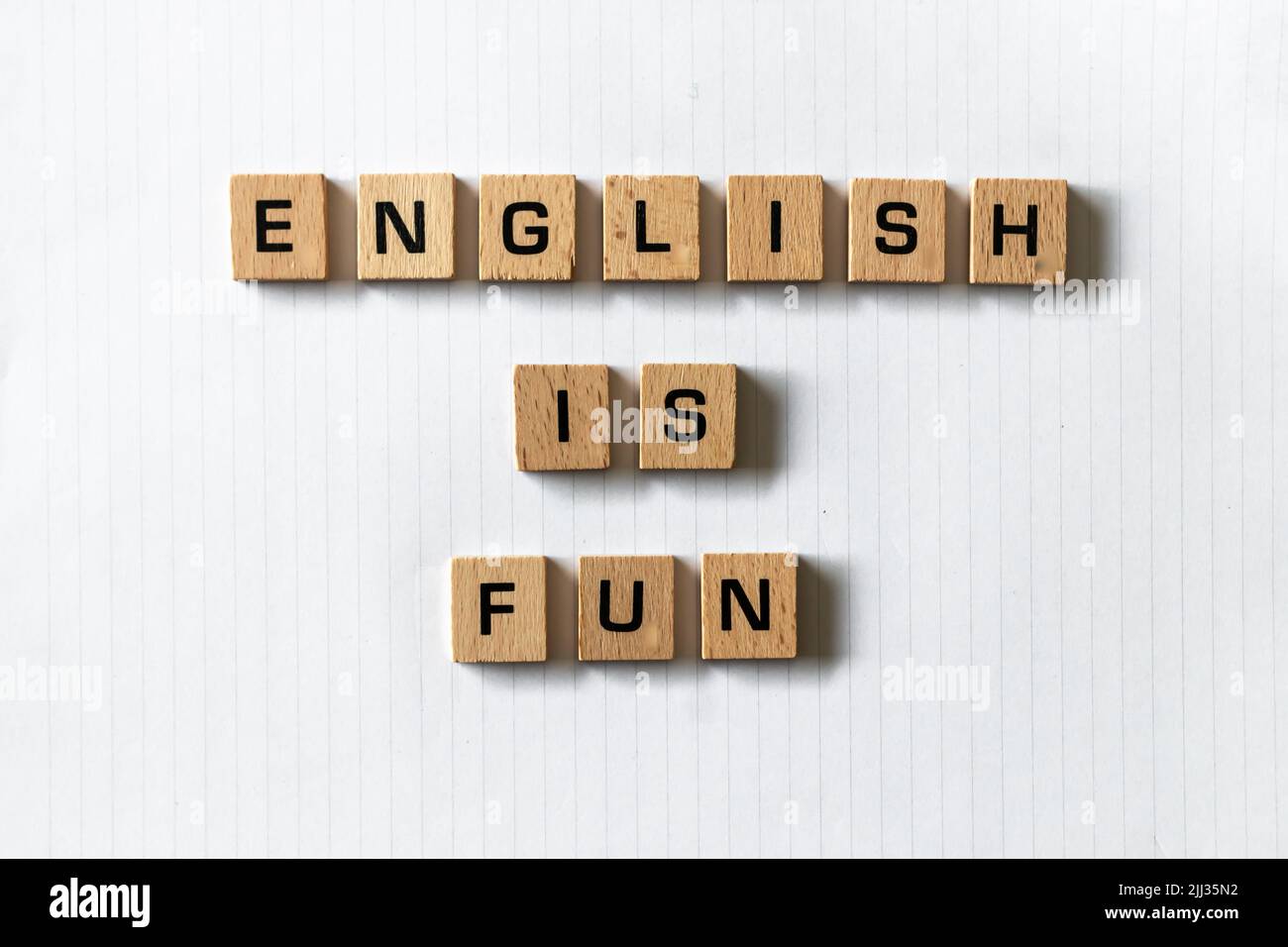 Auf einem weißen, weißen Notizblock wird in Holzbuchstaben „Englisch macht Spaß“ geschrieben. Schreibtischoberfläche aus Hartholz. Zurück in die Schule, persönlich lernen, online lernen. Stockfoto