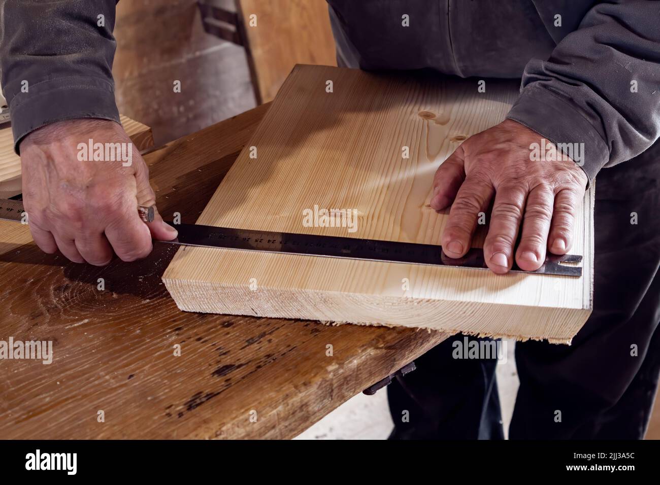 Ein Zimmermann zeichnet in seiner heimischen Werkstatt mit einem Lineal und Bleistift ein Holzbrett aus. Er arbeitet mit Holz. Stockfoto