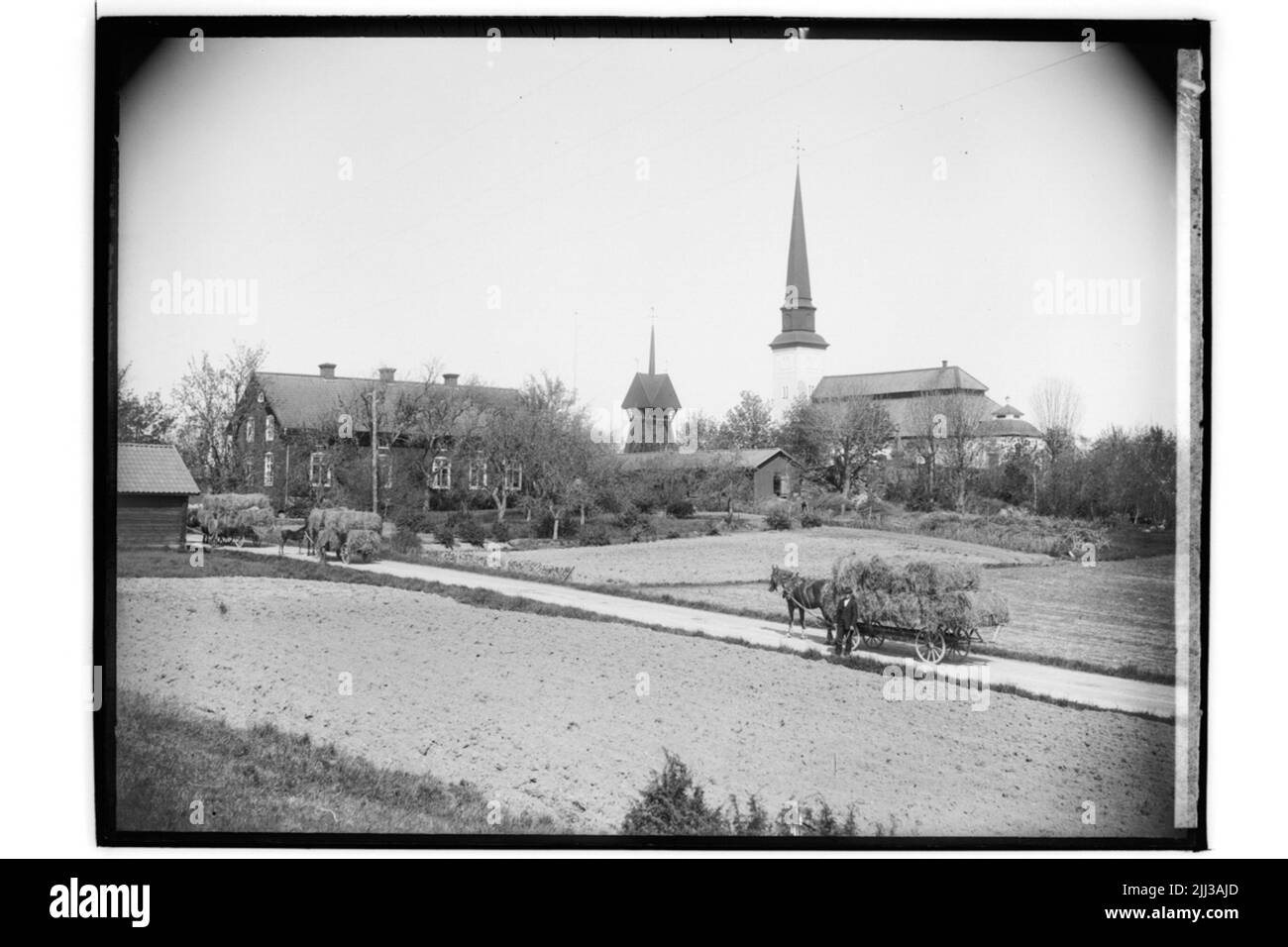 Glanshammars Kirche. Ein halbstöckiges Schulgebäude links von der Kirche. Drei Stroh auf der Straße. GR-102. Stockfoto