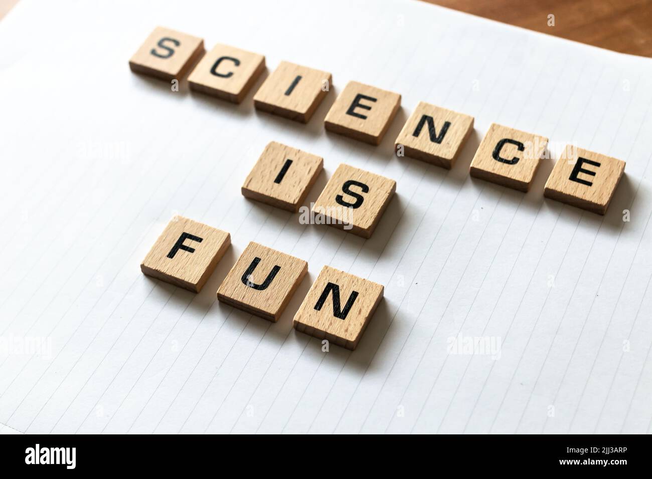 ​ Holzbuchstaben buchstabieren „Wissenschaft macht Spaß“ auf einem weißen, weißen Notizblock. Schreibtischoberfläche aus Hartholz. Zurück in die Schule, persönlich lernen. Stockfoto