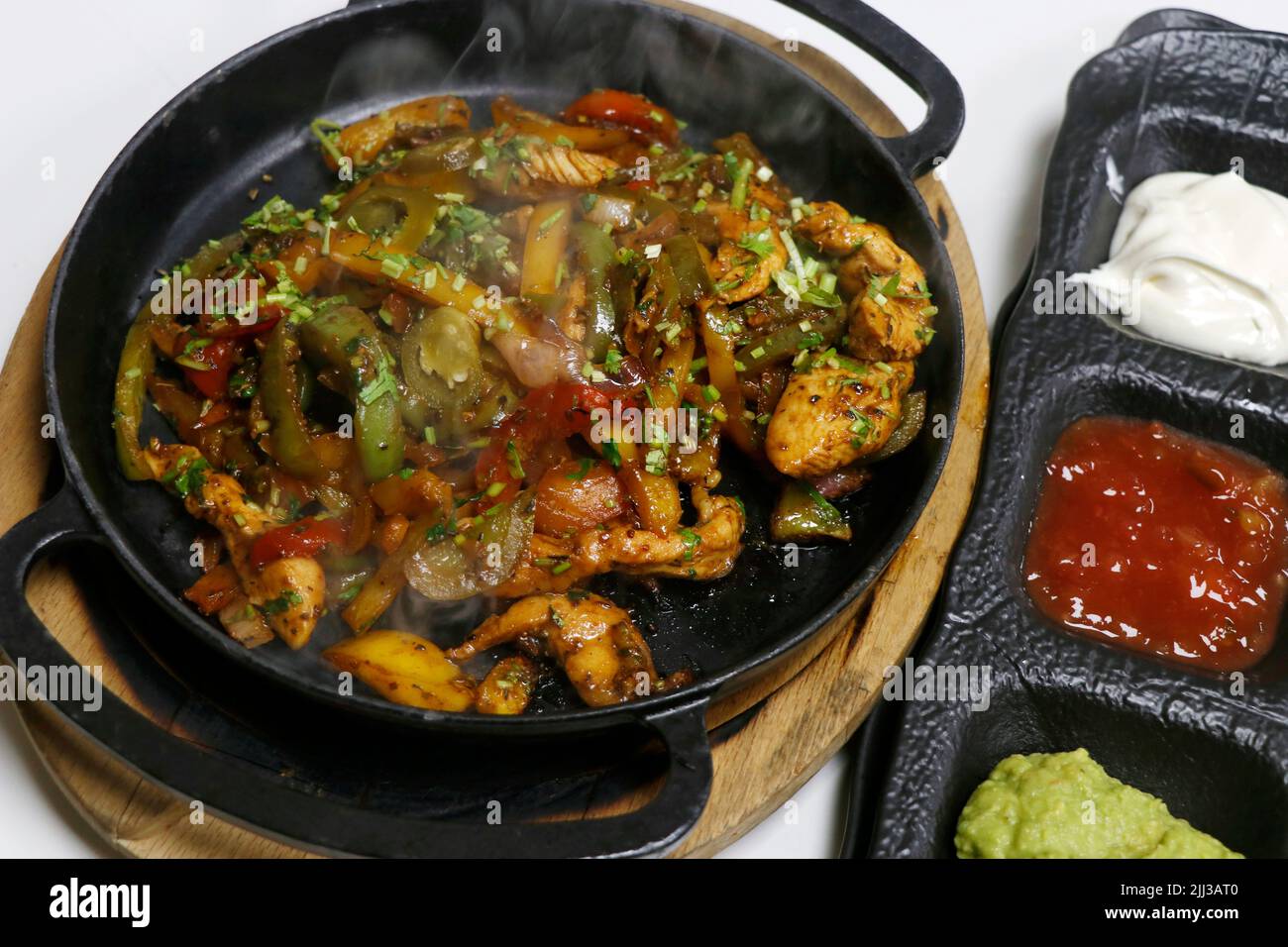 mexikanisches Essen, Chicken Fajitas auf einem heißen, rauchenden Teller mit saurer Creme, Avocado-Guacamole, Tomatensalsa und Tortilla-Brot Stockfoto