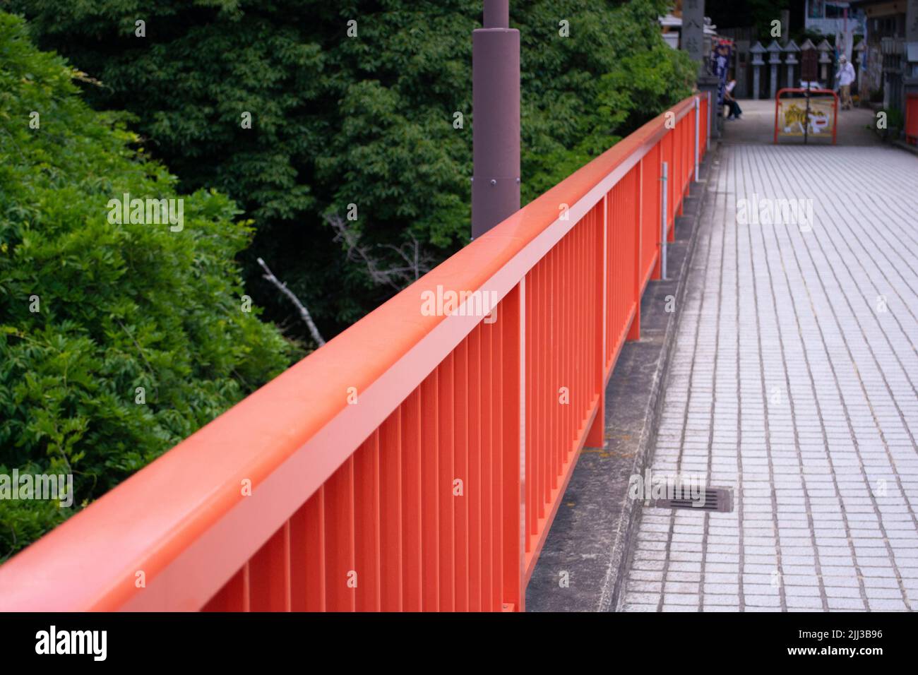 Roter Handlauf auf einer großen Fußgängerbrücke über den Regenwald in Japan. Stockfoto