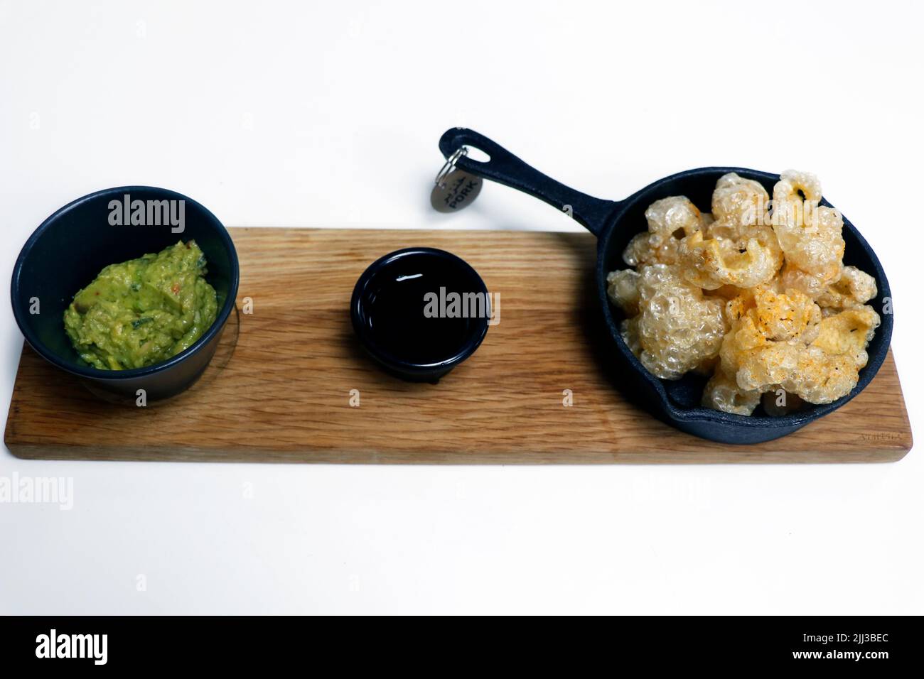 Frittierte knusprige Schweinefleischhaut, auch Chicharon genannt, mit Sojasauce und Avocado Guacamole, philippinischer Delikatesse, serviert einen Teller mit Schweinefleisch-Tag zur Identifizierung Stockfoto