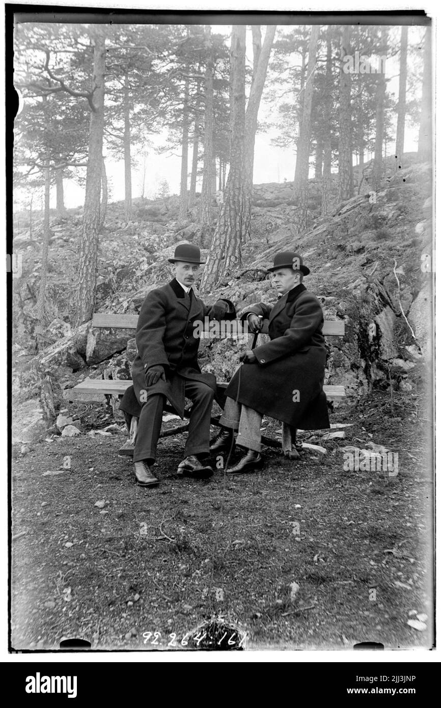 Hålahult Sanatorium, außen, zwei Männer sitzen auf einer Bank im Wald, in Anzug über Rock Hut gekleidet. Stockfoto