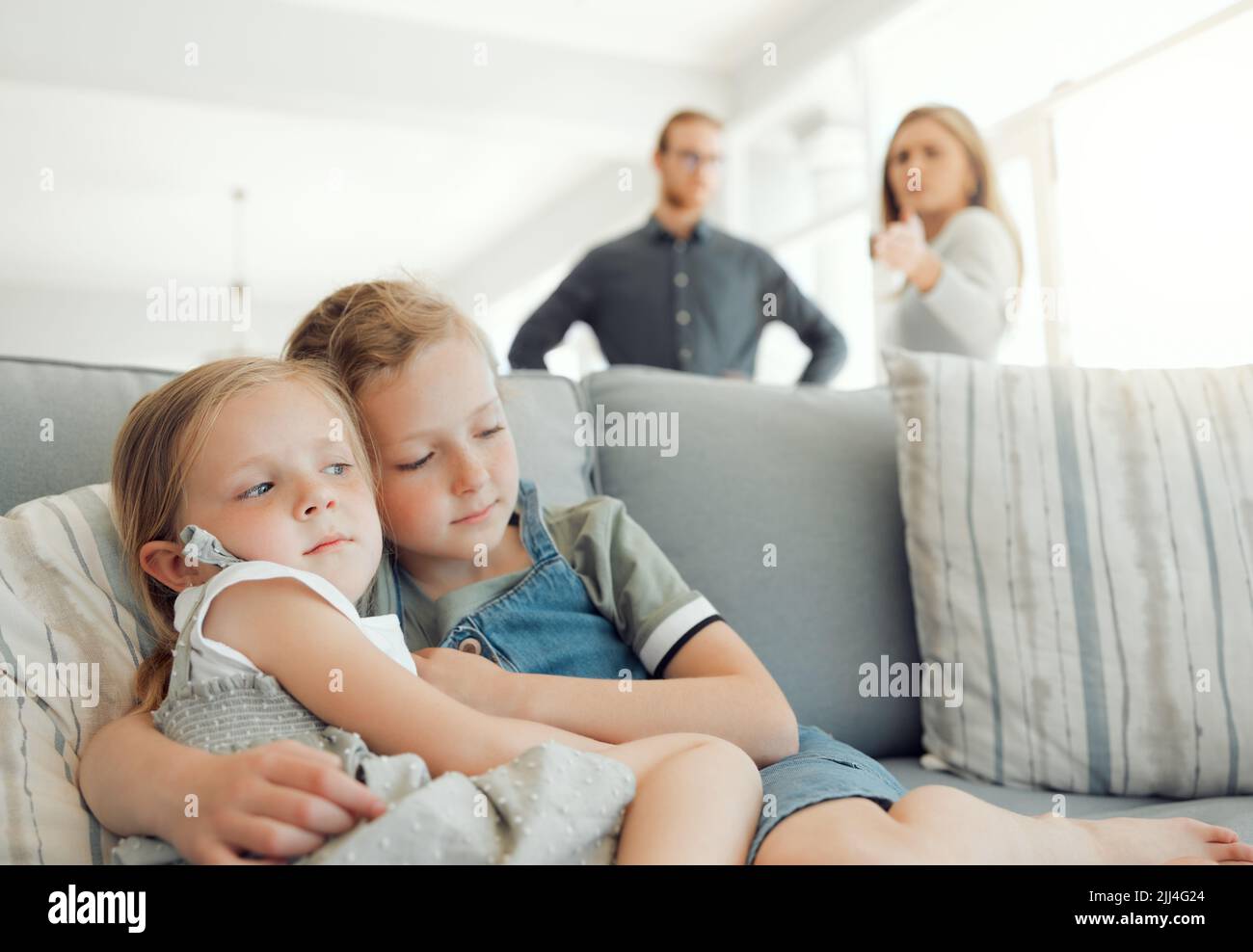 Schauen Sie sich an, was Sie mit ihnen tun. Zwei kleine Mädchen halten sich gegenseitig, während ihre Eltern im Hintergrund zu Hause streiten. Stockfoto