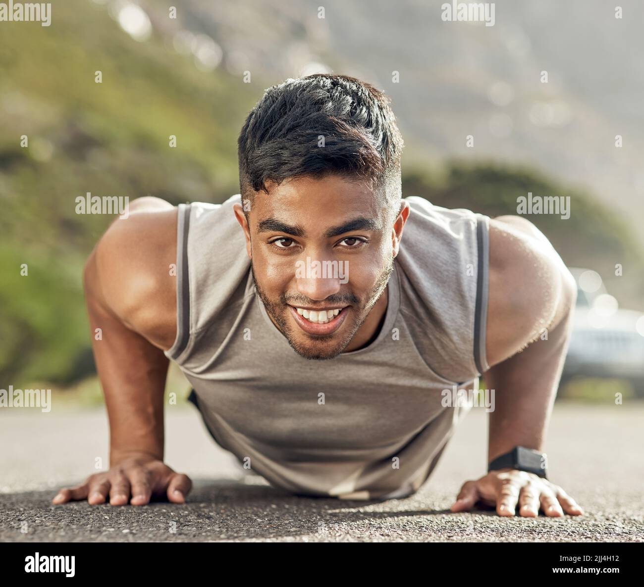 Je mehr du es tust, desto erträglicher wird es. Ein sportlicher junger Mann, der Liegestütze draußen macht. Stockfoto