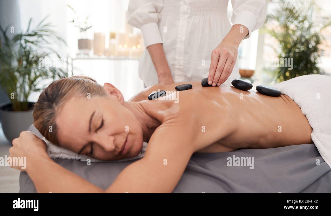 Jeder Stein bringt Harmonie und einen positiven Energiefluss. Eine reife Frau genießt eine entspannende Hot Stone Massage in einem Spa. Stockfoto