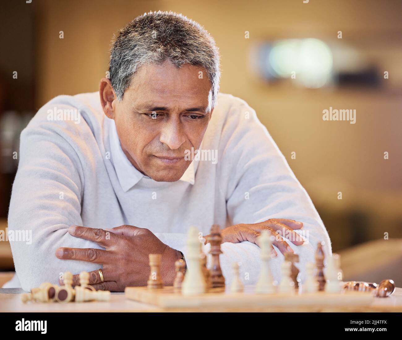 Mein Gegner ist wirklich gut. Ein reifer Mann, der allein drinnen sitzt und nachdenklich schaut, während er ein Schachspiel spielt. Stockfoto