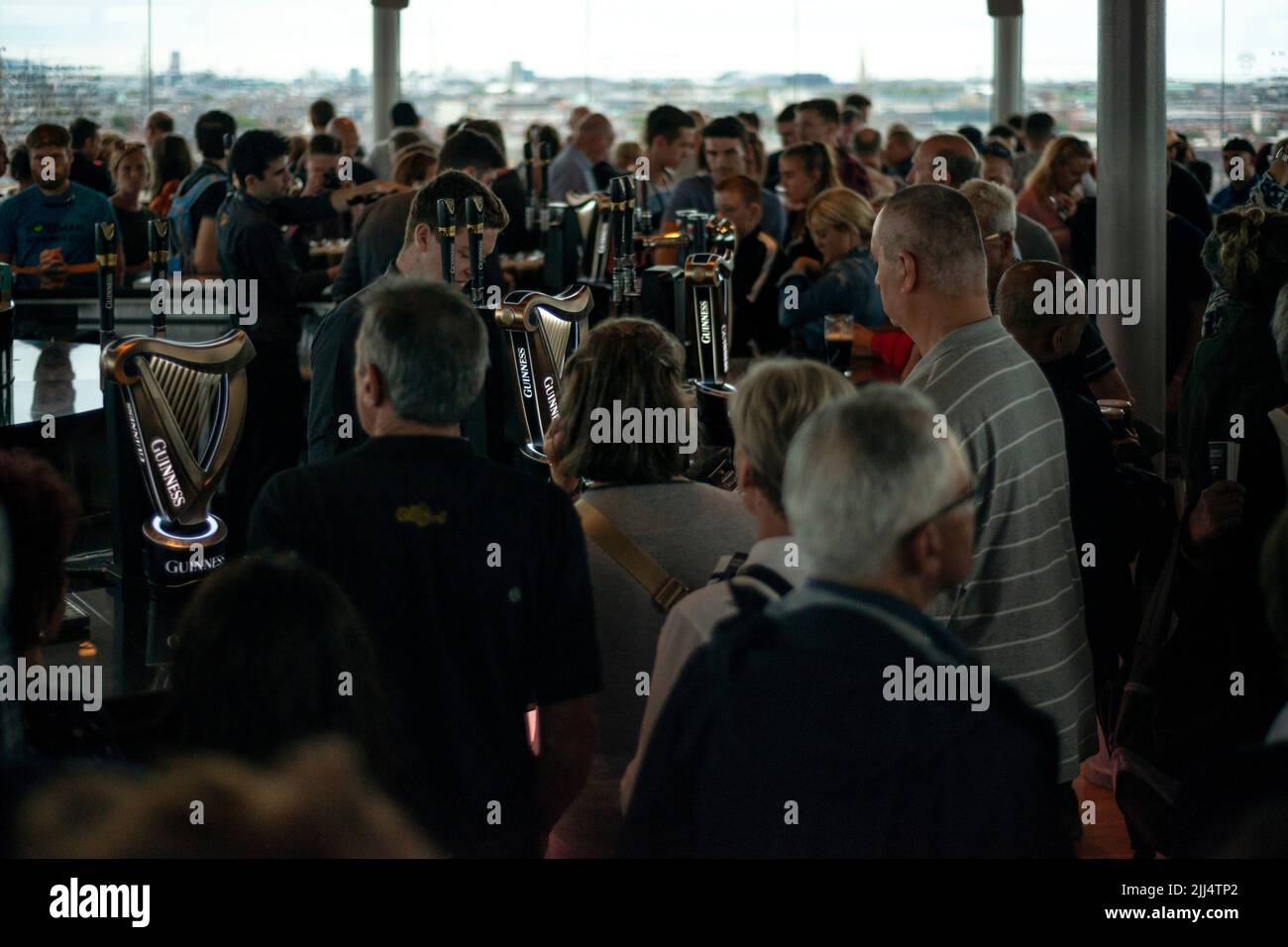 Dunkel und launisch in der Gravity Bar im Guinness Storehouse, Dublin, Irland. Gäste, die sich an der geschäftigen Bar mit Guinness Stout herumbewegen. Trinkkonzept. Stockfoto