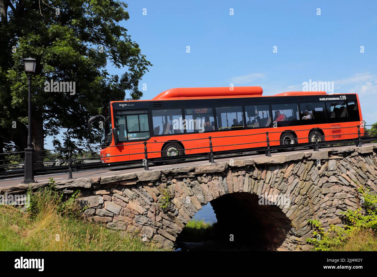 Karsltad, Schweden - 20. Juli 2022: Roter Stadtbus M.A.N über die alte Steinbogenbrücke aus dem 17.. Jahrhundert. Stockfoto