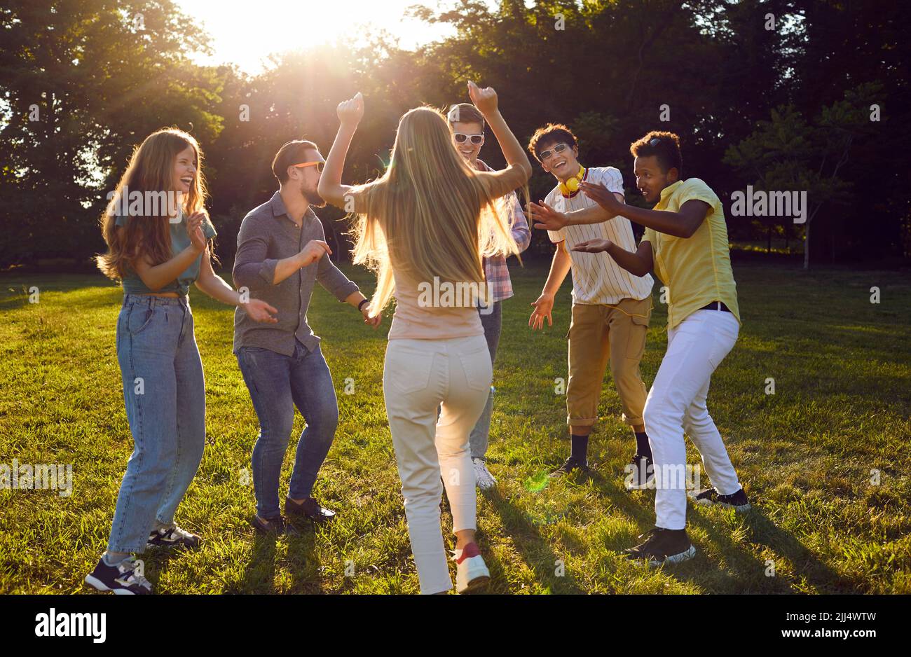 Lustige Gruppe junger Freunde, die am Sommerabend auf dem grünen Rasen im Park tanzen. Stockfoto