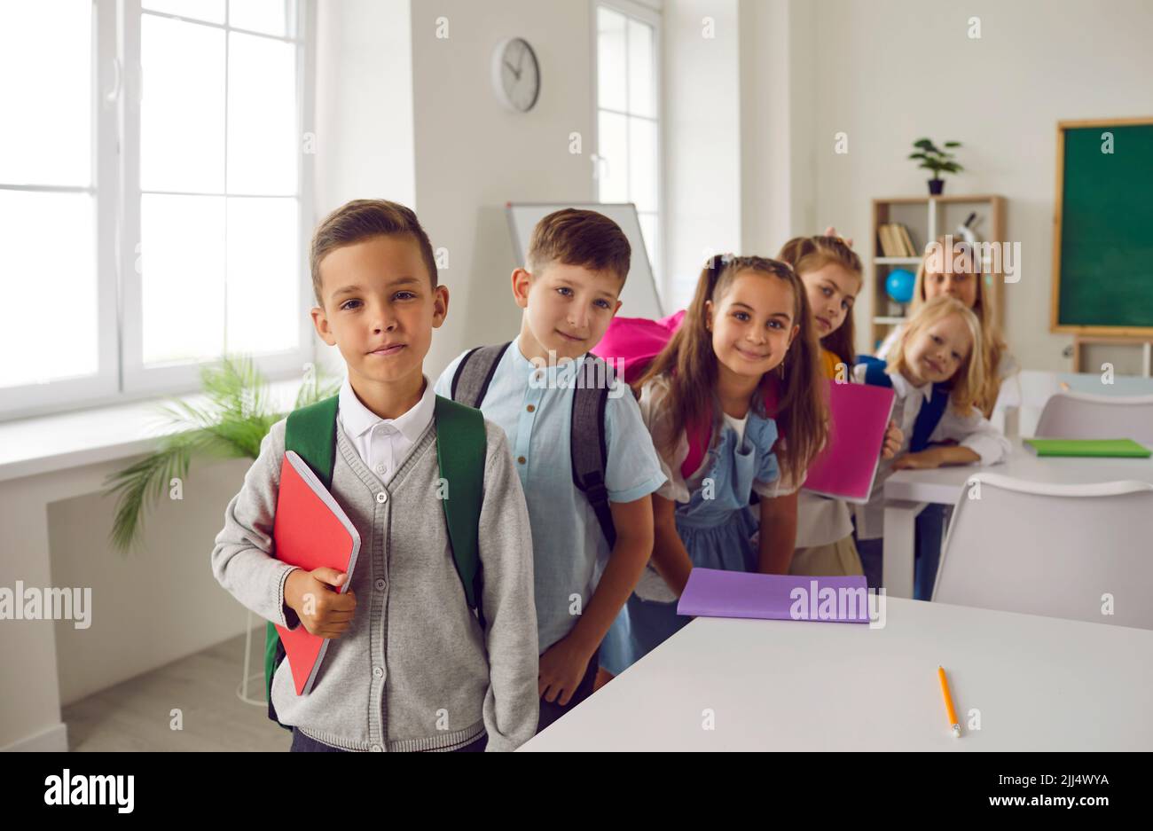 Fröhliche niedliche Grundschüler posieren im Klassenzimmer am 1. September. Stockfoto