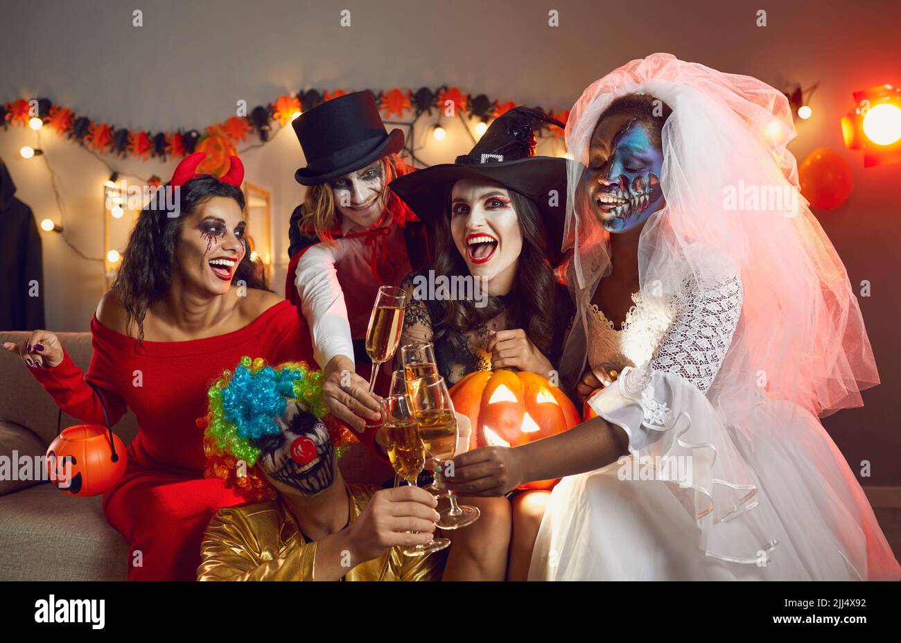 Fröhliche junge Menschen in gruseligen Kostümen trinken und Spaß haben auf der Halloween Party Stockfoto