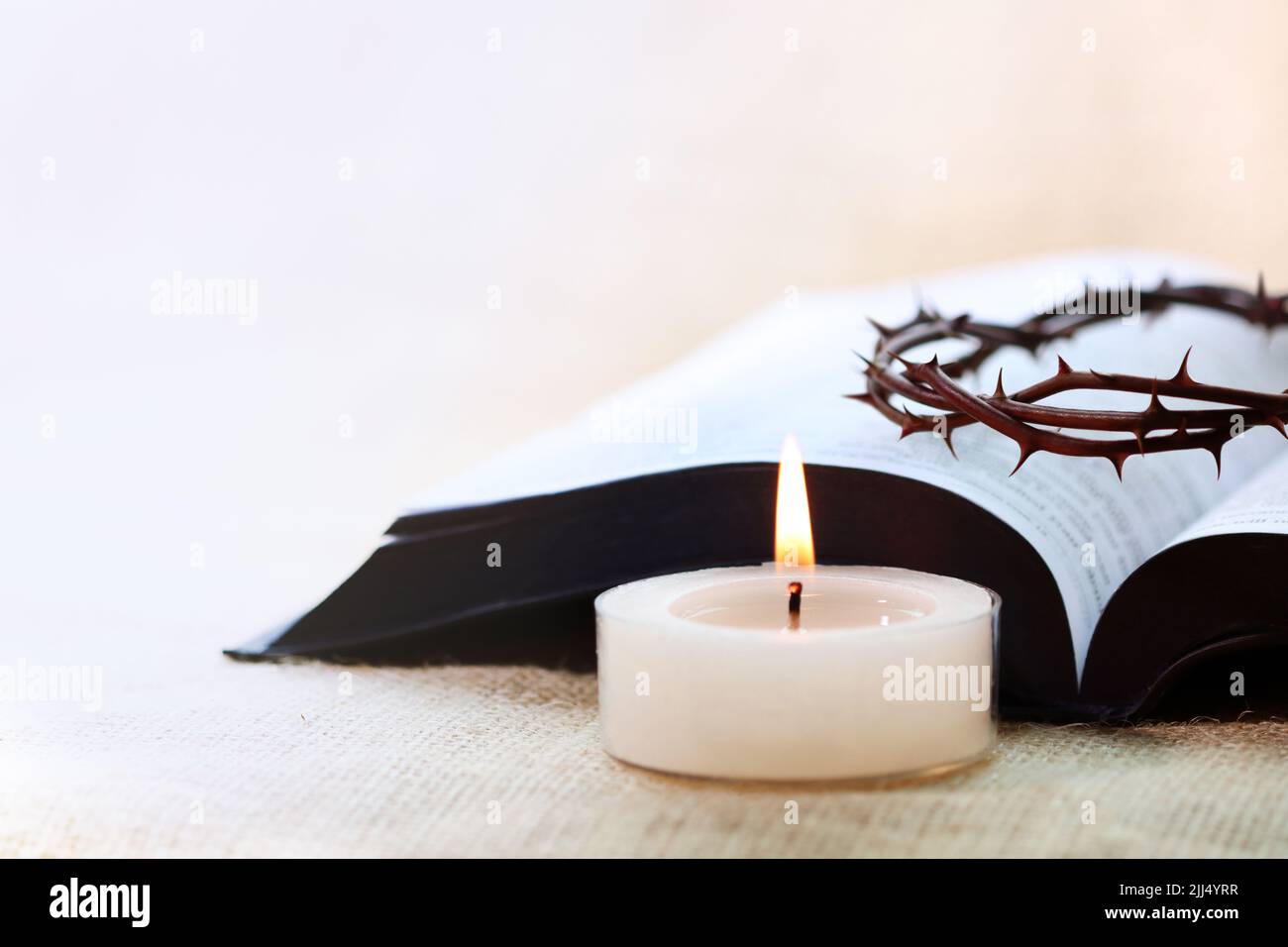Eine hell leuchtende Kerze, eine Dornenkrone, die die Kreuzigung Jesu Christi symbolisiert, und die Heilige Bibel Stockfoto