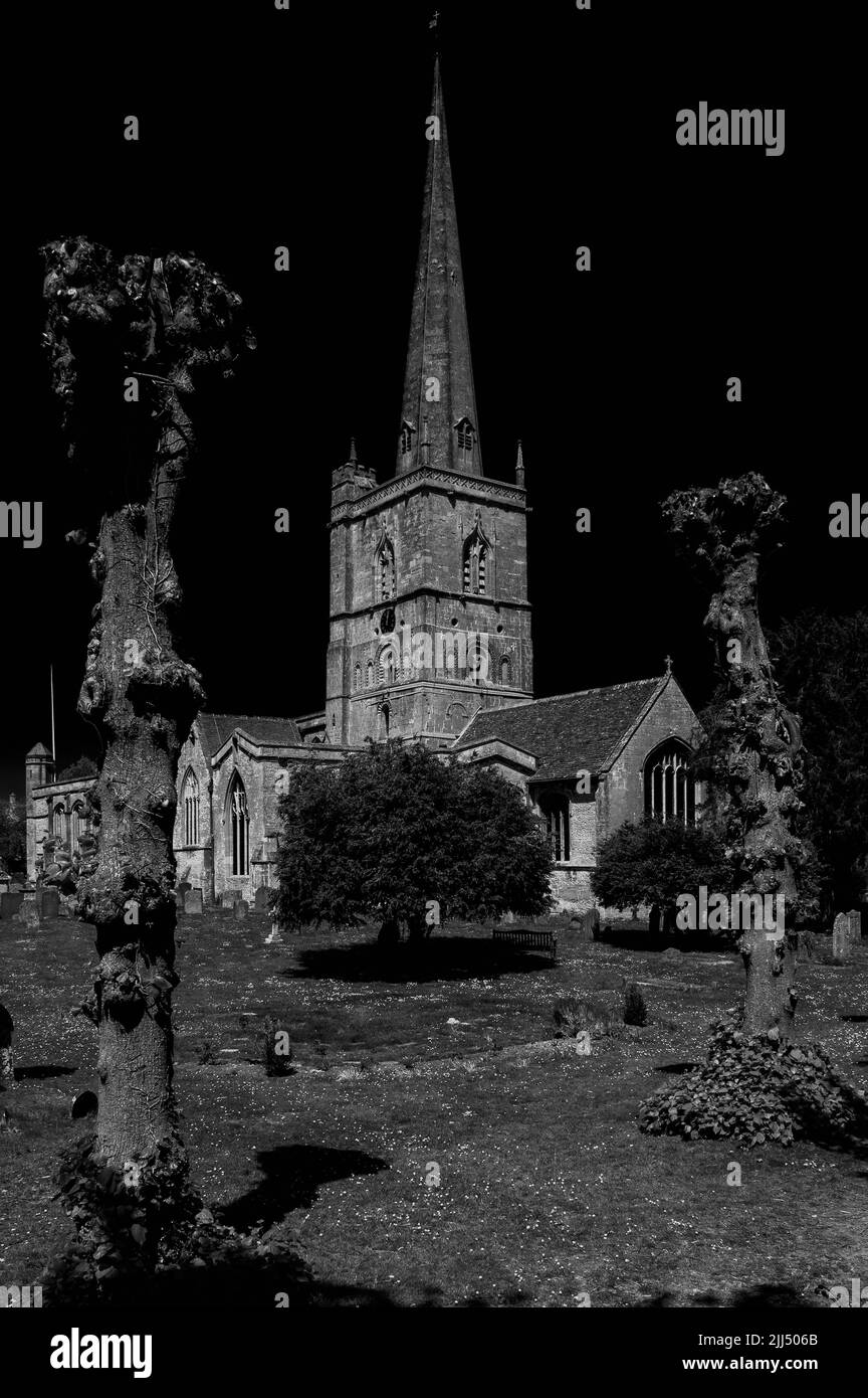 Schwarzweißblick auf die mittelalterliche „Wollkirche“ von St. John dem Täufer in Burford, in den Oxfordshire Cotswolds, England. Die Kirche wurde 1125 gegründet, mit ihrem normannischen Turm erhöht und einem anmutigen Turm Ende der 1400s Jahre hinzugefügt. Im Mai 1649 wurden drei Anführer der Leveller-Meuterei innerhalb der neuen Parlamentsarmee auf Befehl des englischen Bürgerkriegsgenerals Oliver Cromwell durch ein Erschießungskommando auf dem Friedhof hingerichtet. Stockfoto