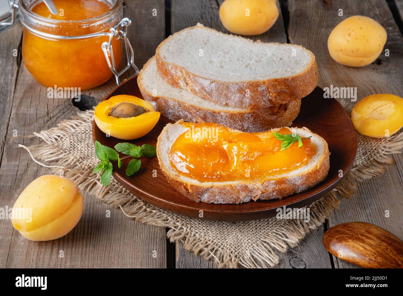 Toast mit Aprikosenmarmelade und frischen Früchten mit Minze auf Holztisch. Stockfoto