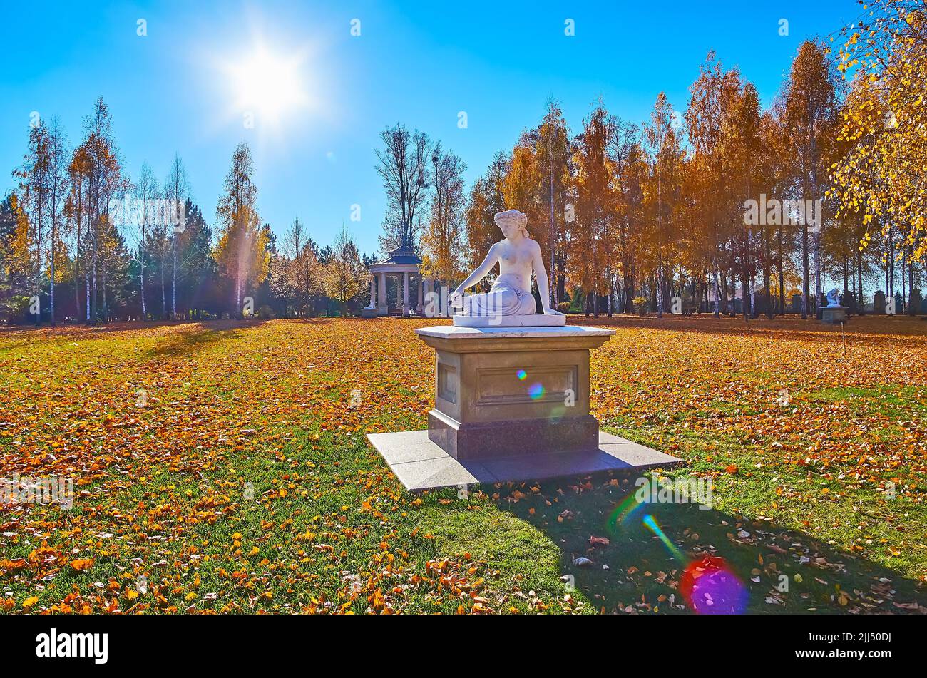 Die Parkskulptur eines Mädchens inmitten der schönen Lichtung mit grünem Gras, gelbem Laub auf dem Hügel und hohen Birken im Hintergrund, Mezhyhirya, Ukrai Stockfoto