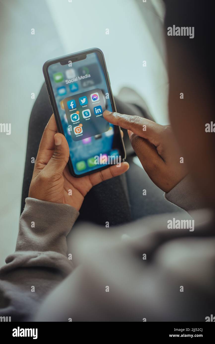Hände einer Person, die ein Mobiltelefon mit Symbolen für soziale Medien auf dem Bildschirm hält Stockfoto