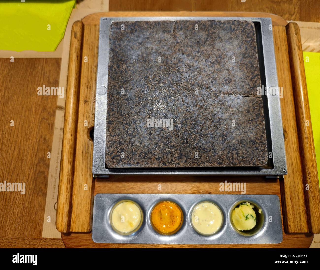 Reinigen Sie den Steingrill auf einem Restauranttisch mit verschiedenen Saucen auf dem Boden. Die Leute können ihr eigenes Fleisch auf den Grill legen Stockfoto