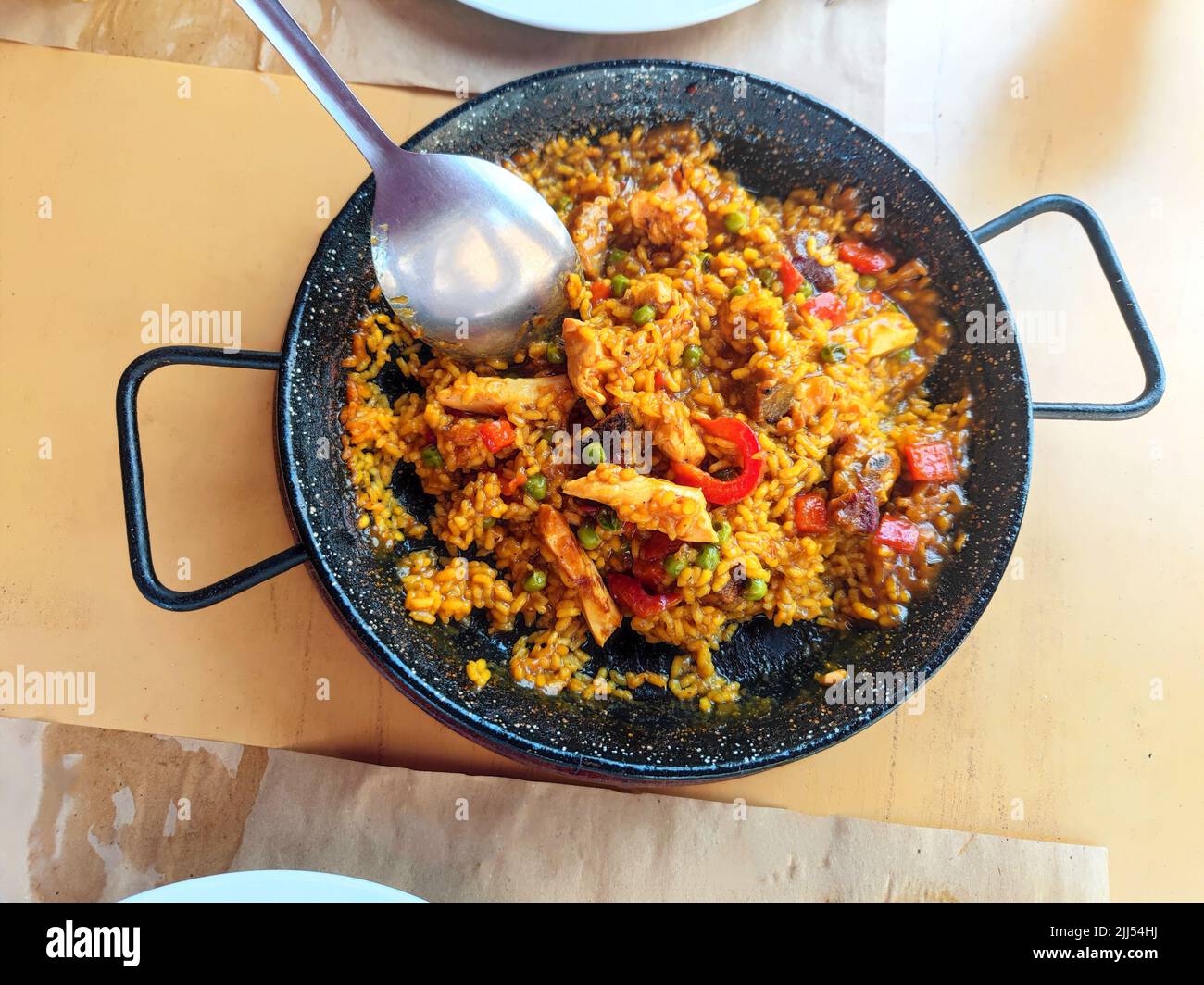 Köstliche Paella-Pfanne mit verschiedenen Gemüse, Huhn und Rindfleisch auf einem Restauranttisch serviert Stockfoto