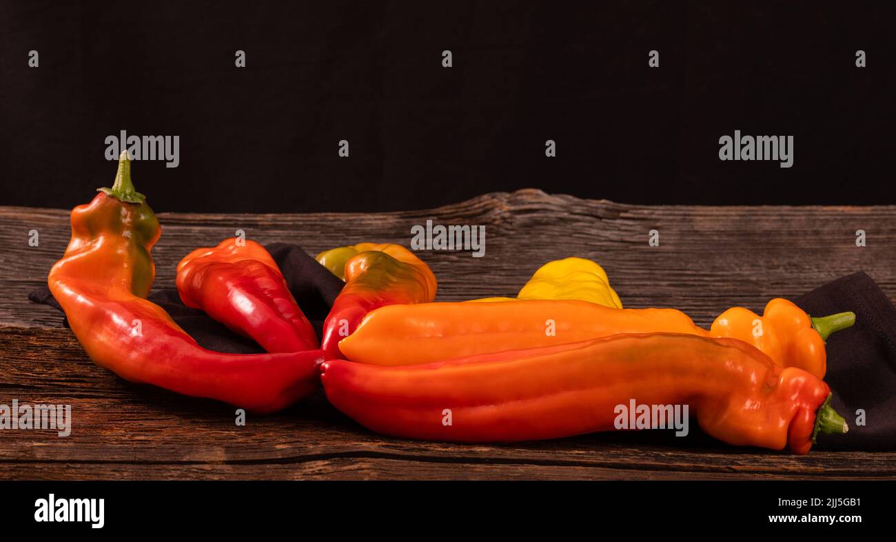 Rote, orange und gelbe lange Paprika auf einem alten rustikalen Holztisch Stockfoto