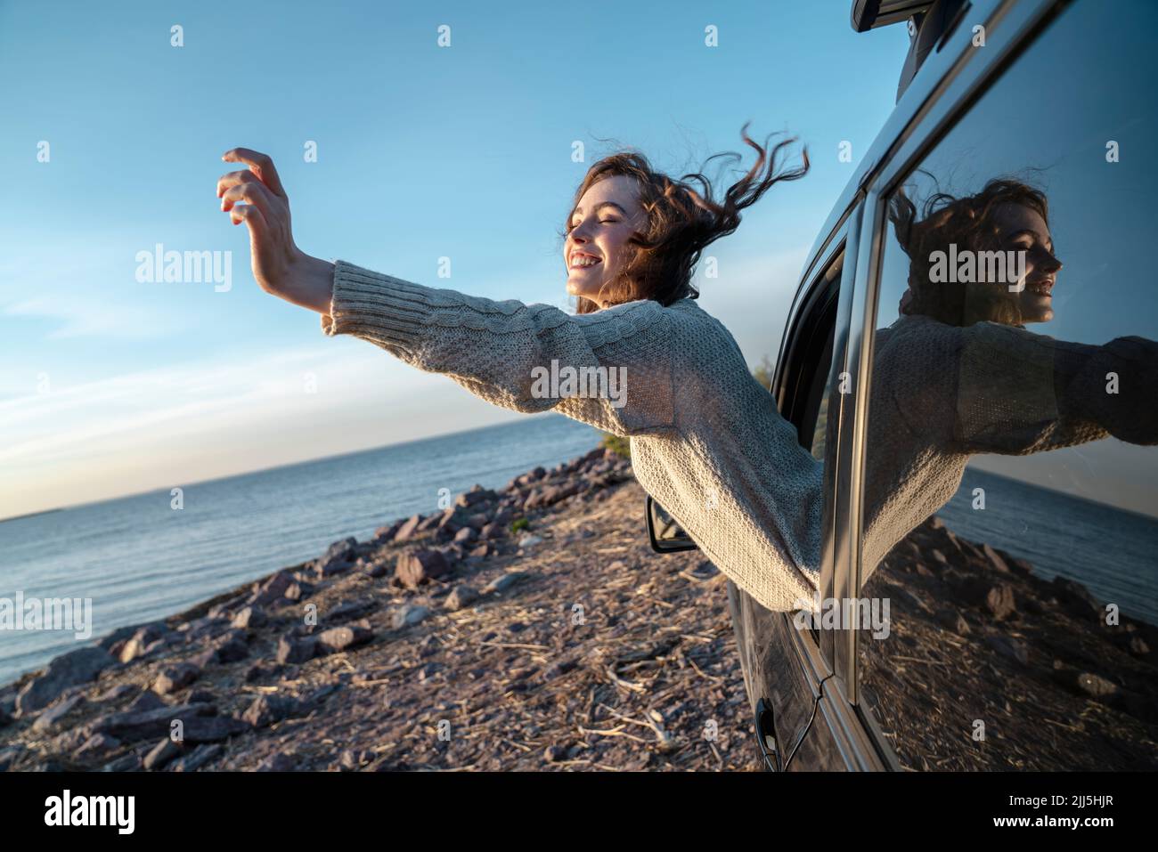 Glückliche junge Frau mit geschlossenen Augen, die sich aus dem Autofenster lehnt Stockfoto