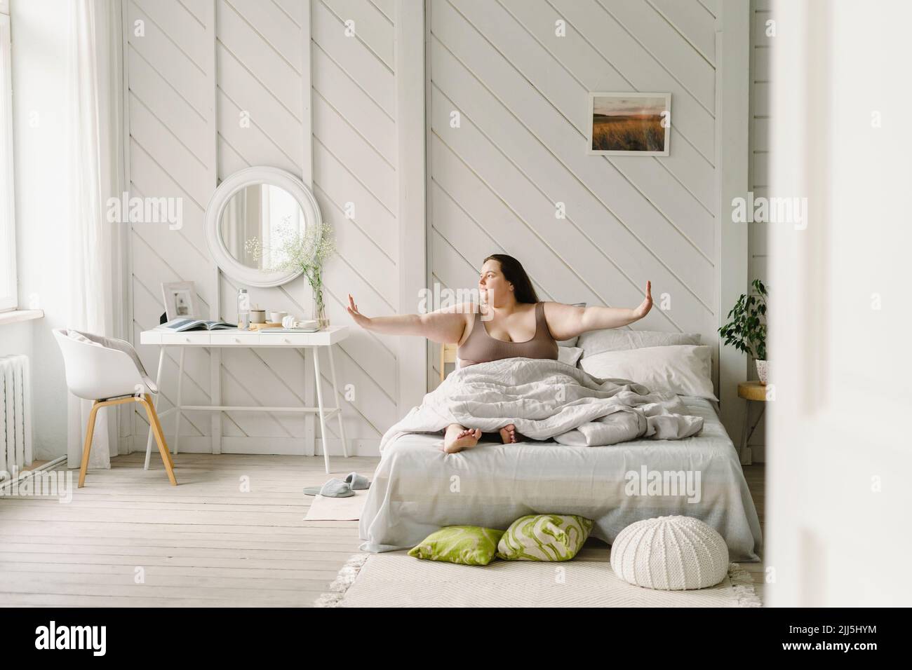 Frau mit ausgestreckten Armen sitzt zu Hause auf dem Bett Stockfoto