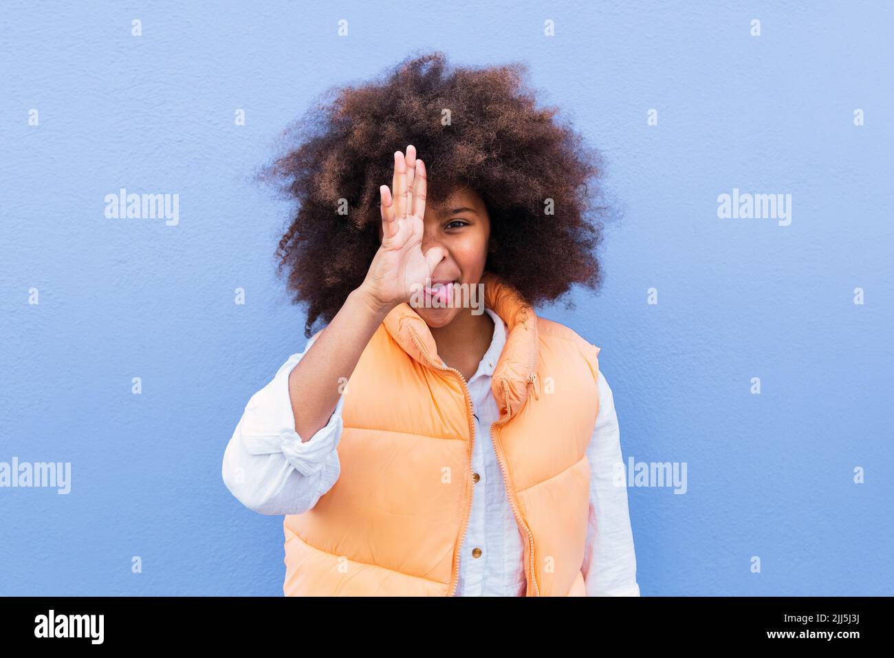 Mädchen mit Afro-Frisur macht lustige Gesicht vor blauem Hintergrund Stockfoto